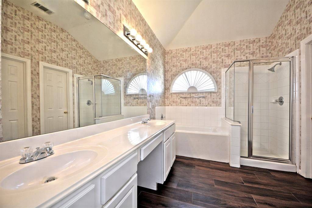 The primary bathroom includes separate his-and-her vanities, a dedicated makeup area, wood tile flooring, and elegant lighting for a bright and functional space.