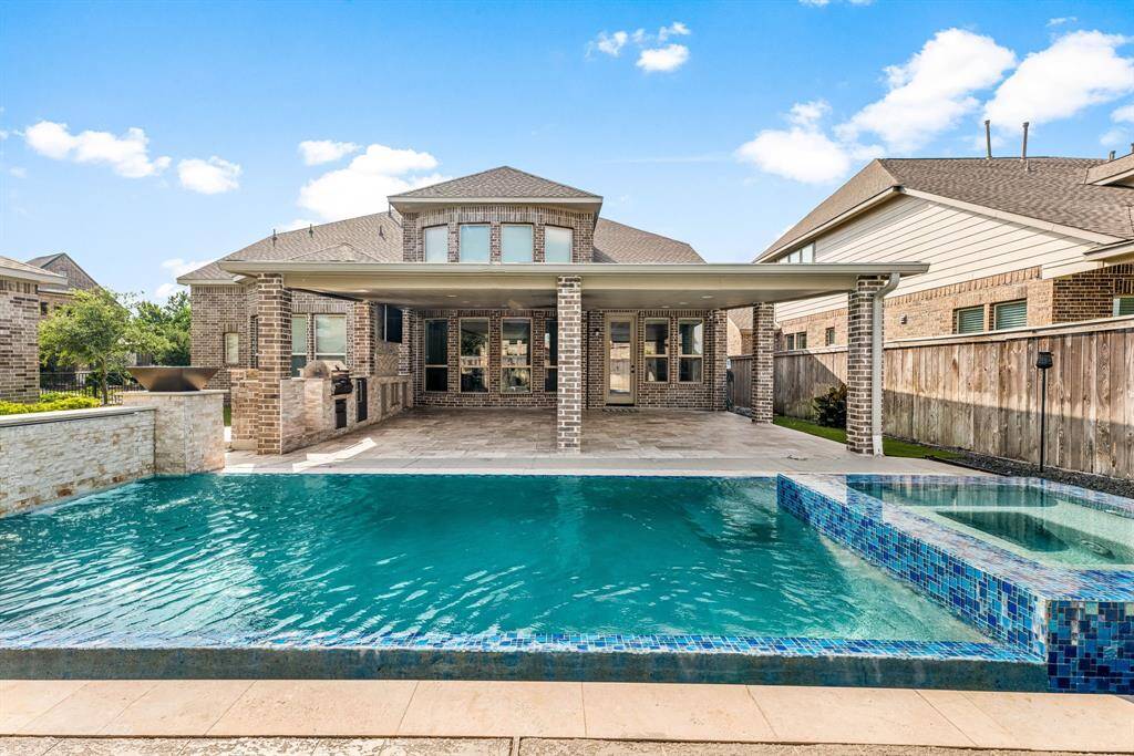This photo showcases a beautiful brick home with a spacious covered patio and a luxurious pool featuring a spa. The outdoor area is perfect for entertaining and relaxation, with ample space and modern amenities.
