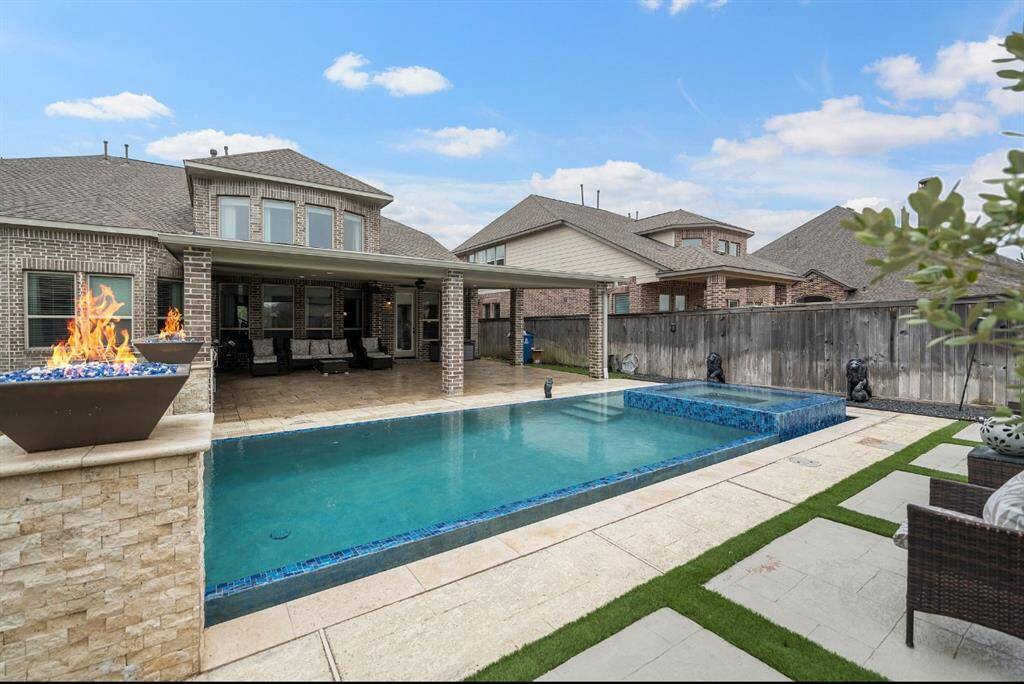 This photo showcases a modern backyard with a sleek swimming pool, elegant fire features, and a spacious covered patio perfect for outdoor entertaining. The brick exterior of the home adds a classic touch, while well-maintained landscaping enhances the inviting atmosphere.