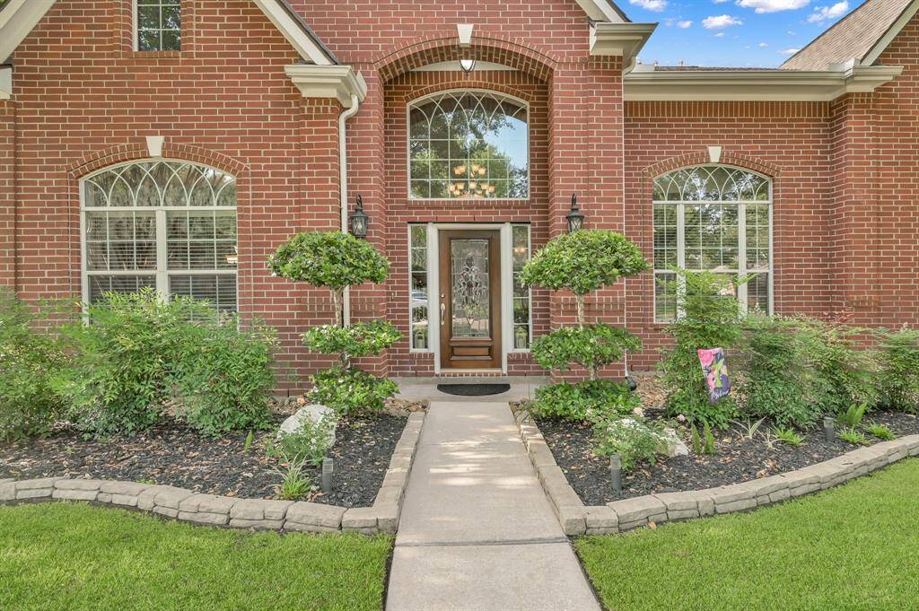 The mature flower beds are lined with stacked pavers. There are arched windows with brick accents, and coach lighting as you enter the covered porch.