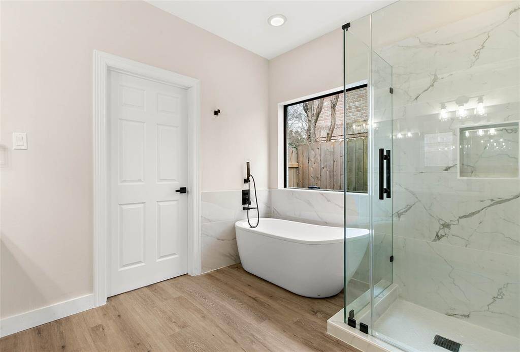 This bathroom features a modern design with a freestanding tub and glass-enclosed shower with marble-style tile.