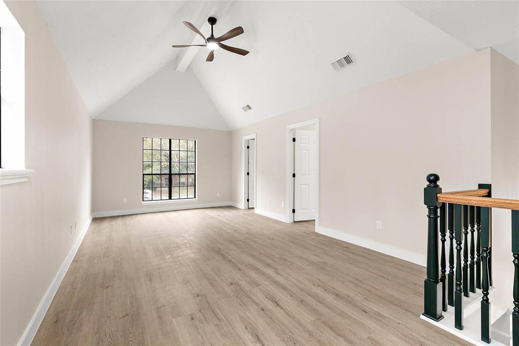 The spacious upstairs game room features vaulted ceilings, a modern ceiling fan, and large windows for natural light.