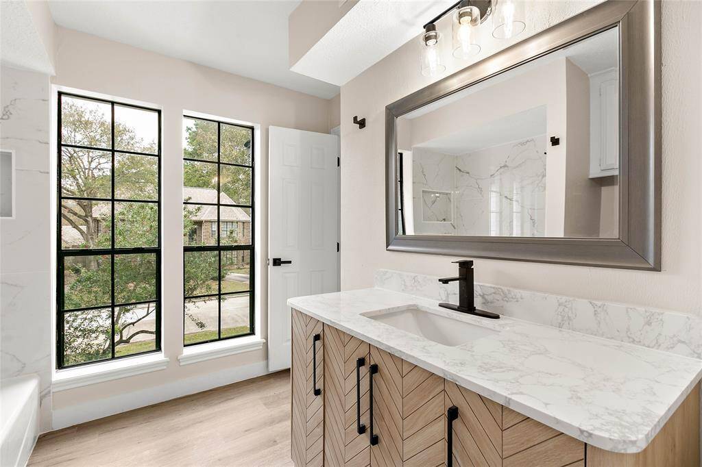 Upstairs bathroom features large windows with black frames offering a view of the outdoors, modern vanity, sleek fixtures, and a large framed mirror.