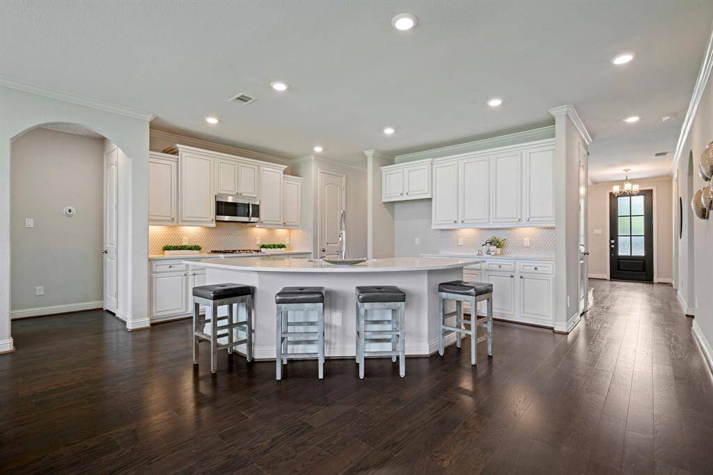 This modern kitchen features elegant white cabinetry, a spacious island with seating and stainless steel appliances.