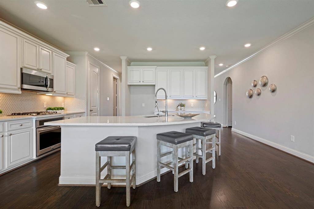 This modern kitchen features elegant white cabinetry, a spacious island with seating and stainless steel appliances.