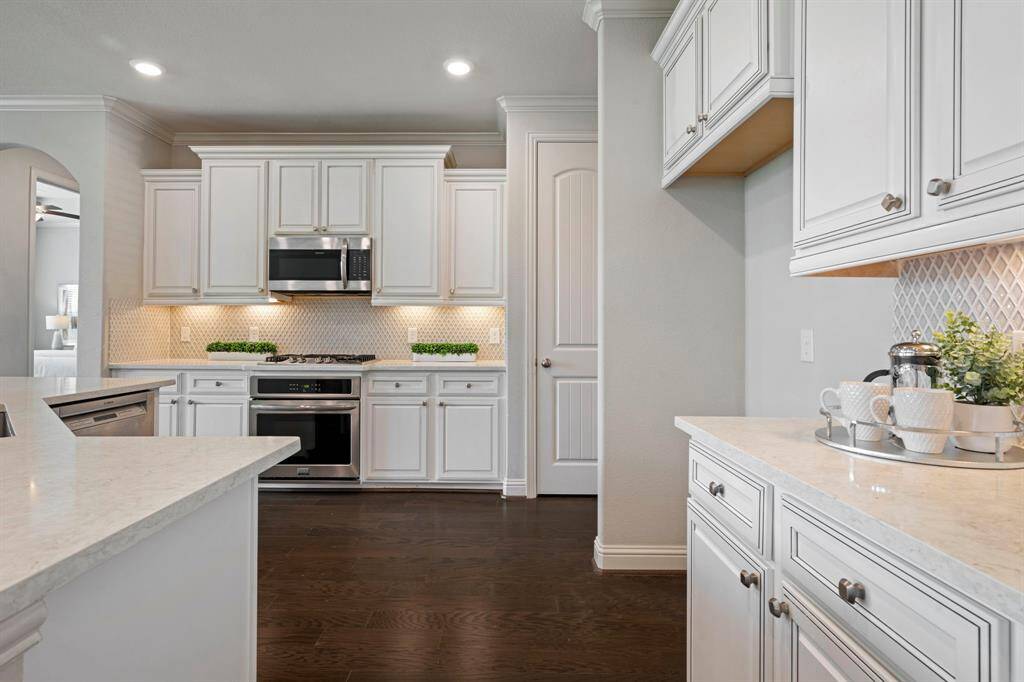 This modern kitchen features elegant white cabinetry, a spacious island with seating and stainless steel appliances.