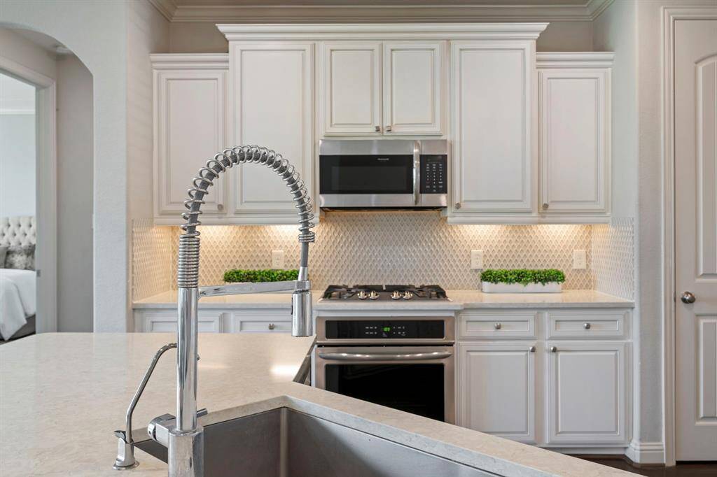 This modern kitchen features elegant white cabinetry, a spacious island with seating and stainless steel appliances.