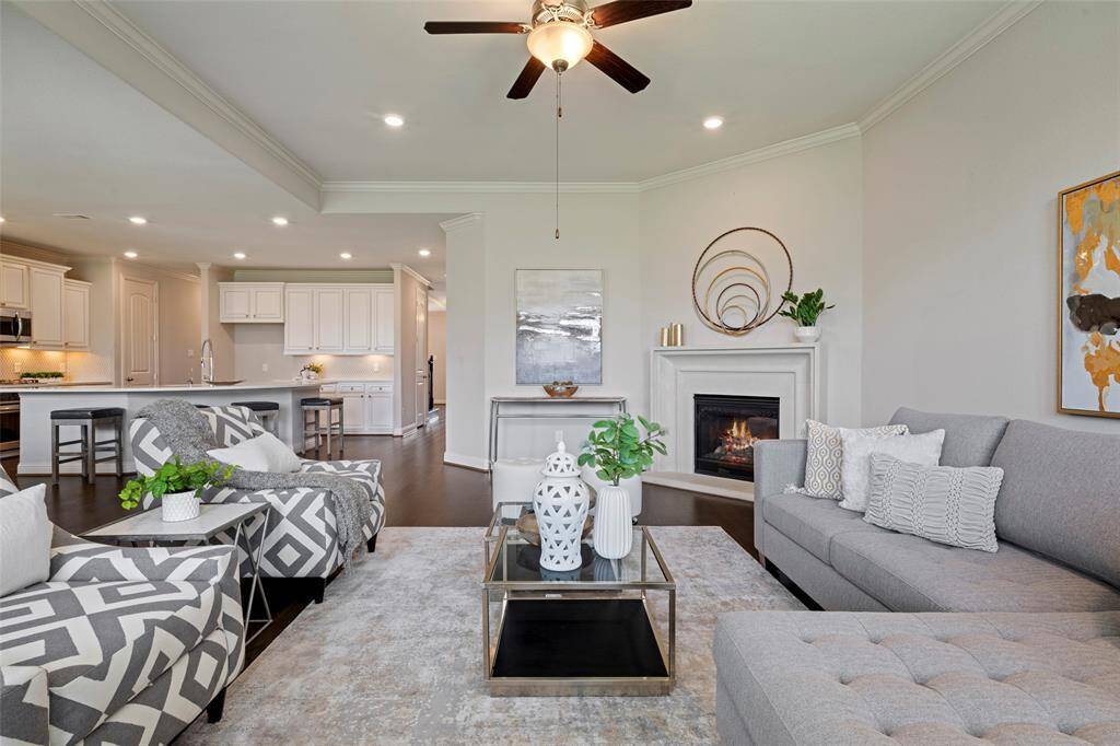 This inviting living room features a cozy fireplace, and large windows that provide ample natural light seamlessly connecting to a contemporary kitchen with sleek cabinetry and a breakfast bar.