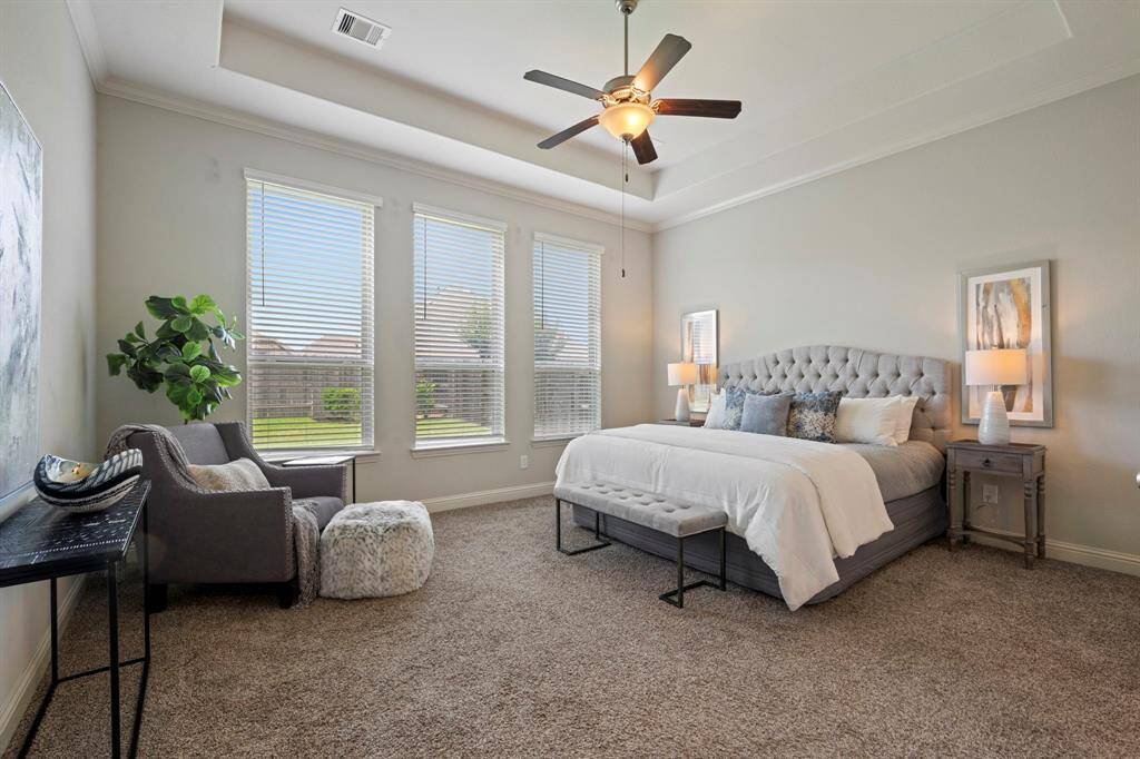 This spacious primary bedroom features a cozy carpeted floor and ample natural light from multiple windows.