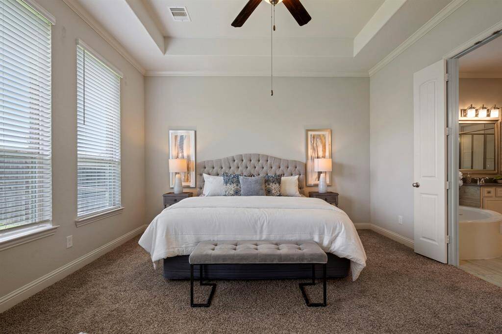 This spacious primary bedroom with large windows that provide ample natural light, and a ceiling fan adding extra comfort. An adjacent door leads to a modern bathroom, enhancing convenience.