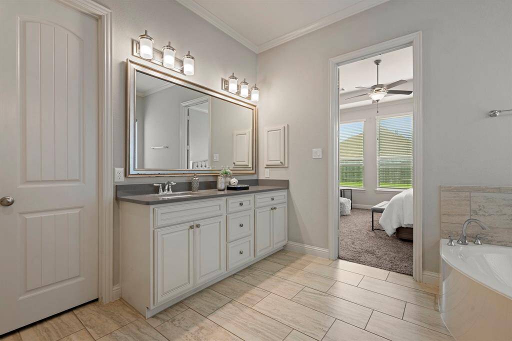 This photo showcases a modern primary bathroom with a double vanity, sleek countertops, and elegant lighting fixtures. A door leads to a cozy bedroom.