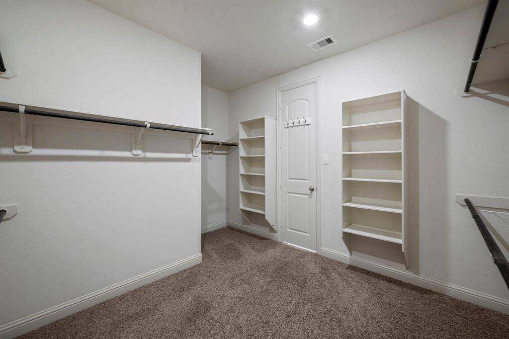 Spacious walk-in closet with ample hanging space, carpeted flooring, and bright overhead lighting.