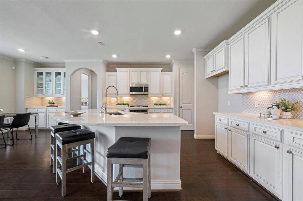 This modern kitchen features elegant white cabinetry, a spacious island with seating and stainless steel appliances.
