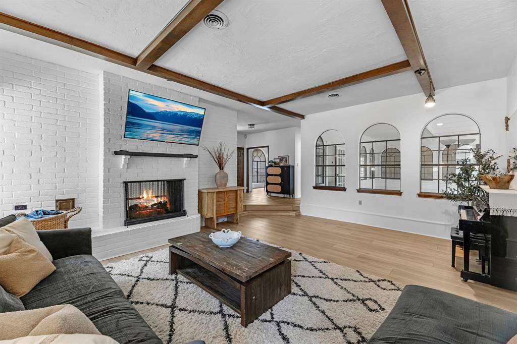 Cozy living room with a painted brick fireplace, wood ceiling beams, and a mounted TV.