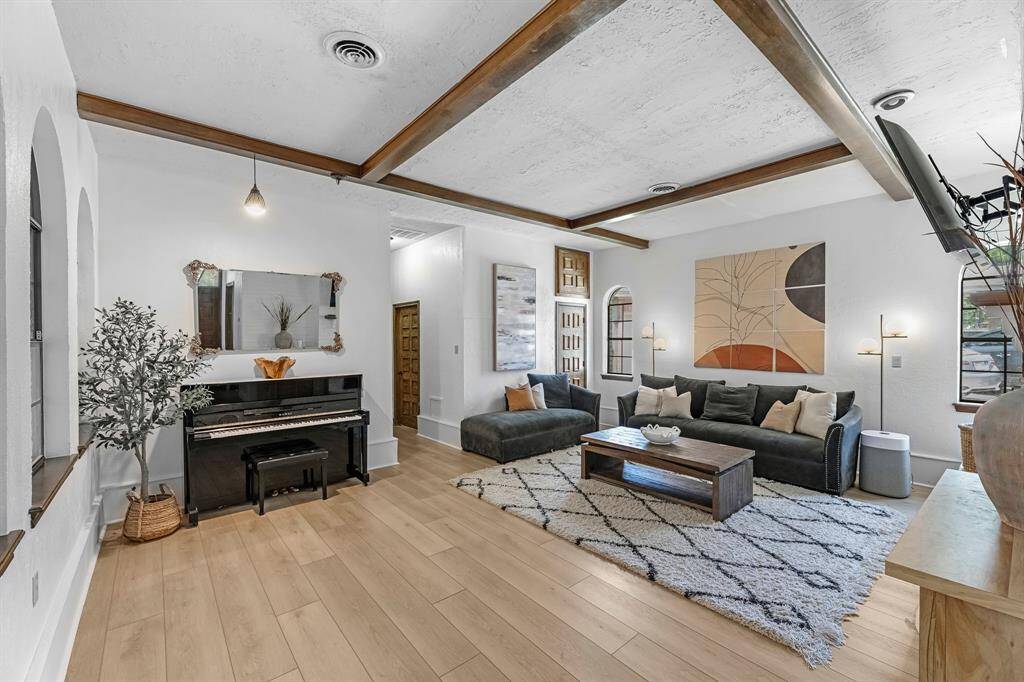 Enjoy refined comfort in this stunning living room showcasing custom wood ceiling beams, arched windows, and a soft, neutral palette. A cozy lounge area is paired with a beautiful piano nook, perfect for entertaining or unwinding. Modern finishes blend seamlessly with timeless charm in this elegant, light-filled space.