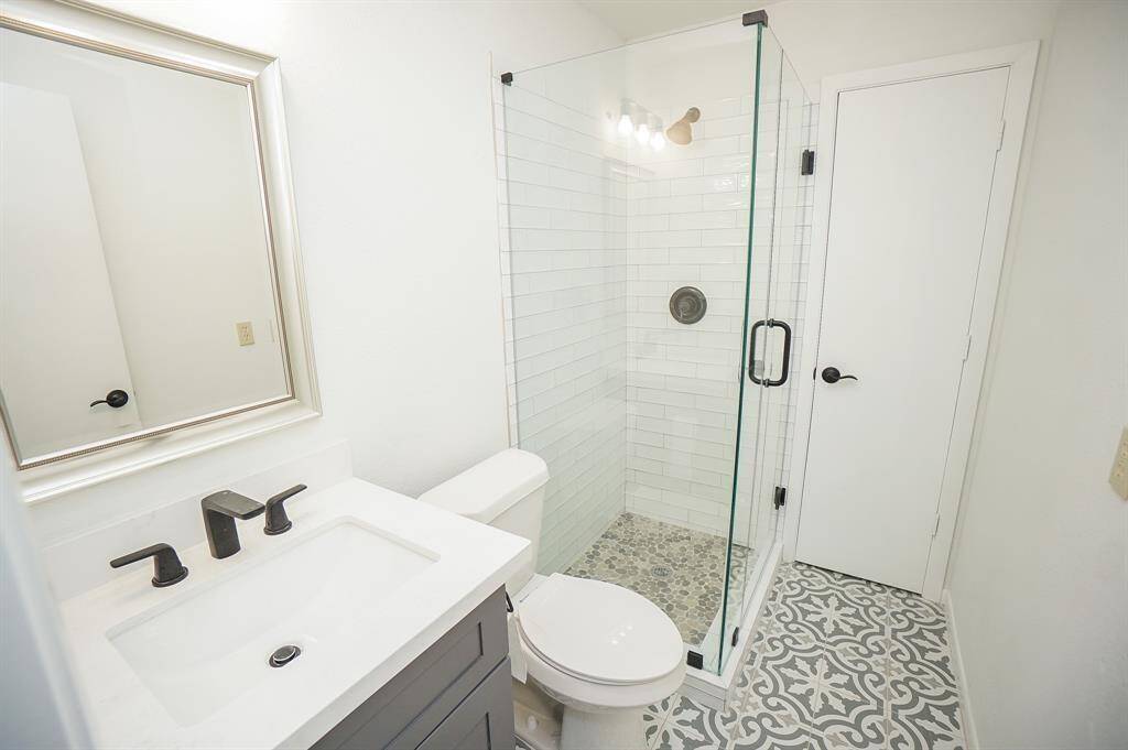 This beautifully remodeled primary bathroom combines modern elegance with functional design. Enjoy the sleek walk-in shower with a frameless glass enclosure, subway tile walls, and pebble stone flooring for a spa-like touch. The updated vanity features a quartz countertop, matte black fixtures, and a framed mirror that adds a hint of sophistication.