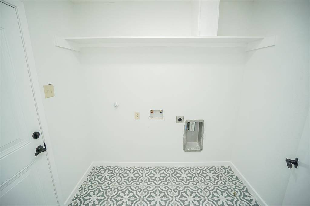 This bright and stylish laundry room offers both charm and functionality! Featuring bold patterned tile flooring and clean white walls, the space feels fresh and modern. A convenient upper shelf provides storage for laundry essentials, while hookups are ready for your washer and dryer. The exterior door offers direct access to the backyard.
