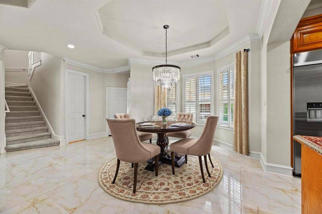 The breakfast area is a sunlit retreat, showcasing an exquisite designer chandelier that adds a touch of glamour. Gracefully curved windows adorned with custom shutters frame the space, creating a warm, inviting ambiance just steps from the gourmet kitchen.