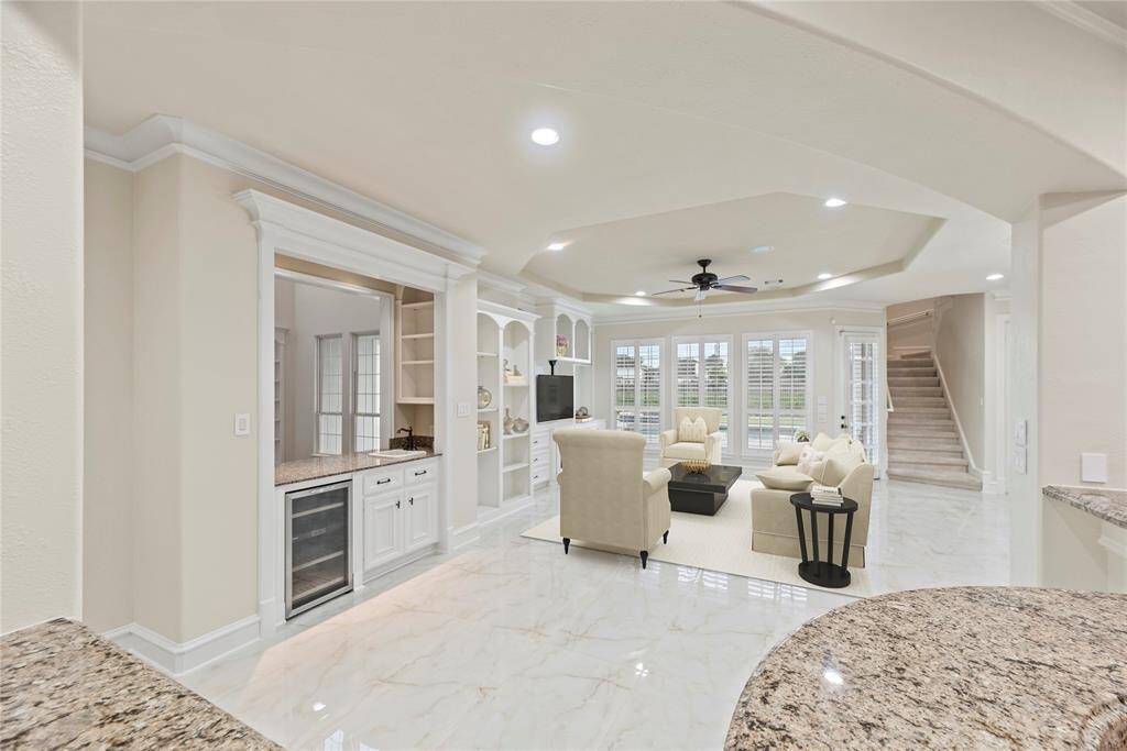 Flowing effortlessly from the kitchen, the inviting living space features custom-built white cabinetry, offering both elegance and functionality. This open-concept design connects to the gourmet kitchen and sunlit sitting space along with the breakfast area, all beneath a beautifully crafted ceiling that adds depth to the space.
