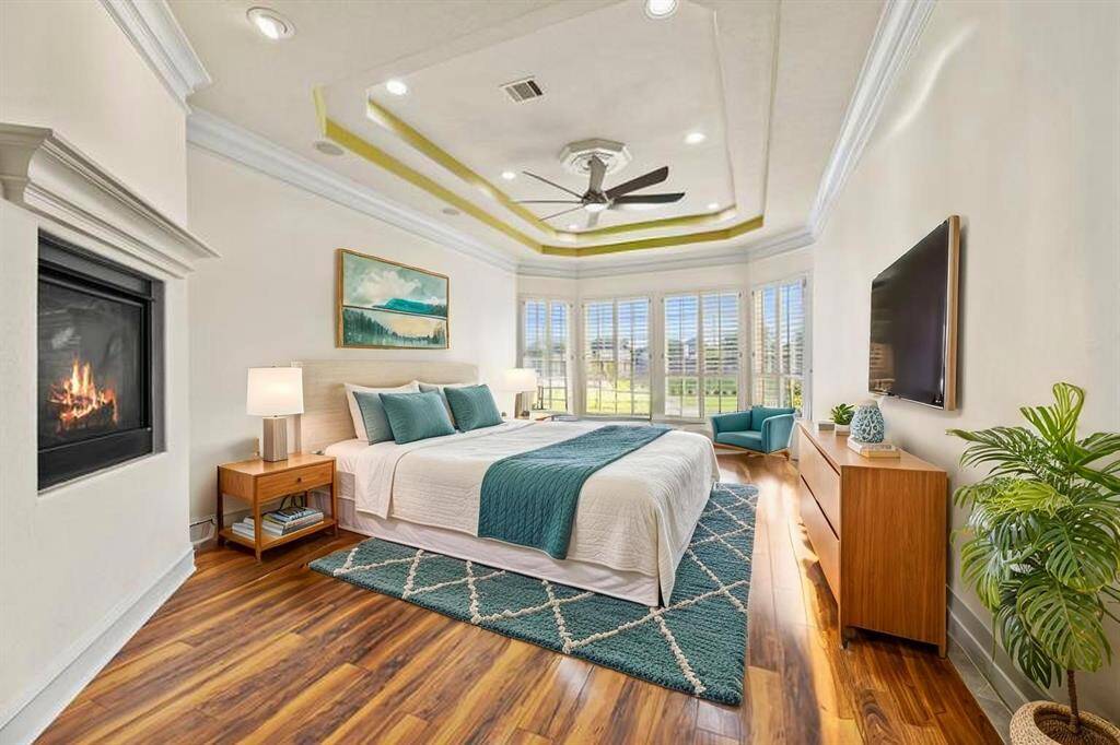 Enter the primary bedroom, a serene retreat distinguished by a dramatic double-trayed ceiling adorned with intricate crown molding. Warm hardwood floors extend beneath a cozy fireplace, while expansive windows frame breathtaking views of the picturesque backyard, inviting natural light to fill the space with tranquil elegance.
