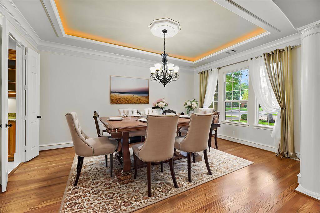 The formal dining room exudes elegance with its trayed, illuminated ceiling, rich hardwood floors, and a statement chandelier that casts a warm, sophisticated glow. A double door entry leads directly to the beautifully appointed butler’s pantry, perfect for effortless entertaining.