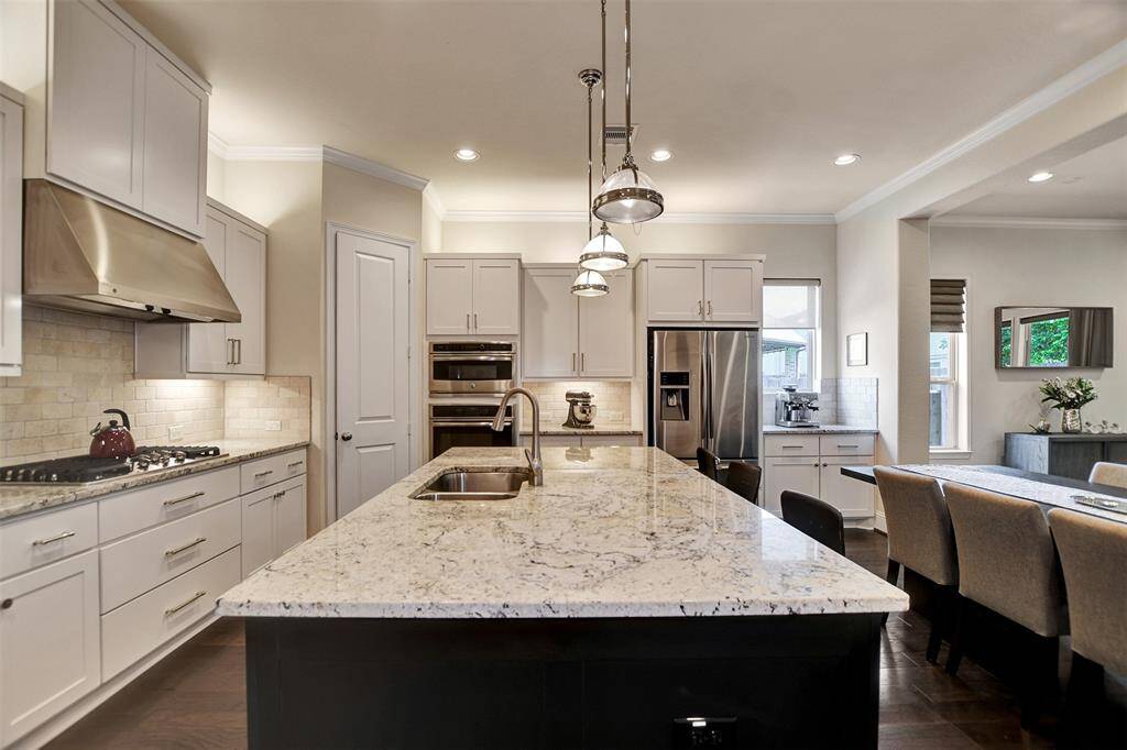 This modern kitchen features sleek white cabinetry, a large island with seating, and elegant lighting. The open layout flows into the living area with ample natural light, perfect for entertaining.