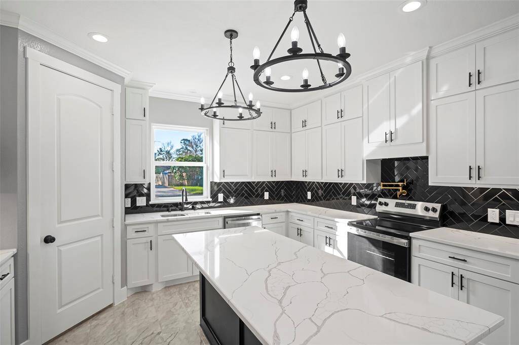 Here you can see beautiful quartz countertops illuminated by pendant lighting fixtures. A large walk-in pantry to the left, and new stainless-steel appliances with a brushed gold pot-filler over the stove.