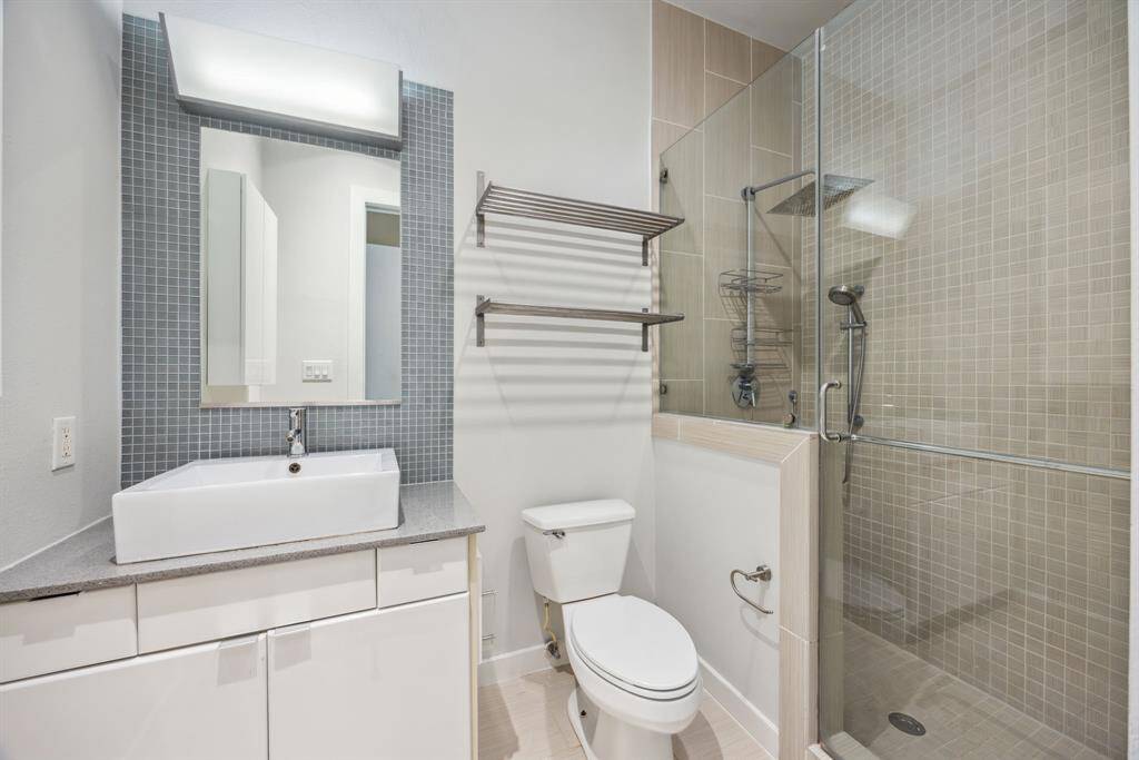 The ensuite bath features a spacious walk in shower, quartz counters, plenty storage, and decorative tile finishes.