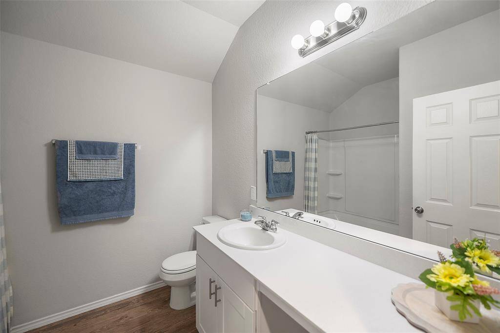 Secondary bathroom features a large mirror with vanity lighting, an extended countertop with a sink, and ample storage space. The area includes a full-sized bathtub with shower combo.