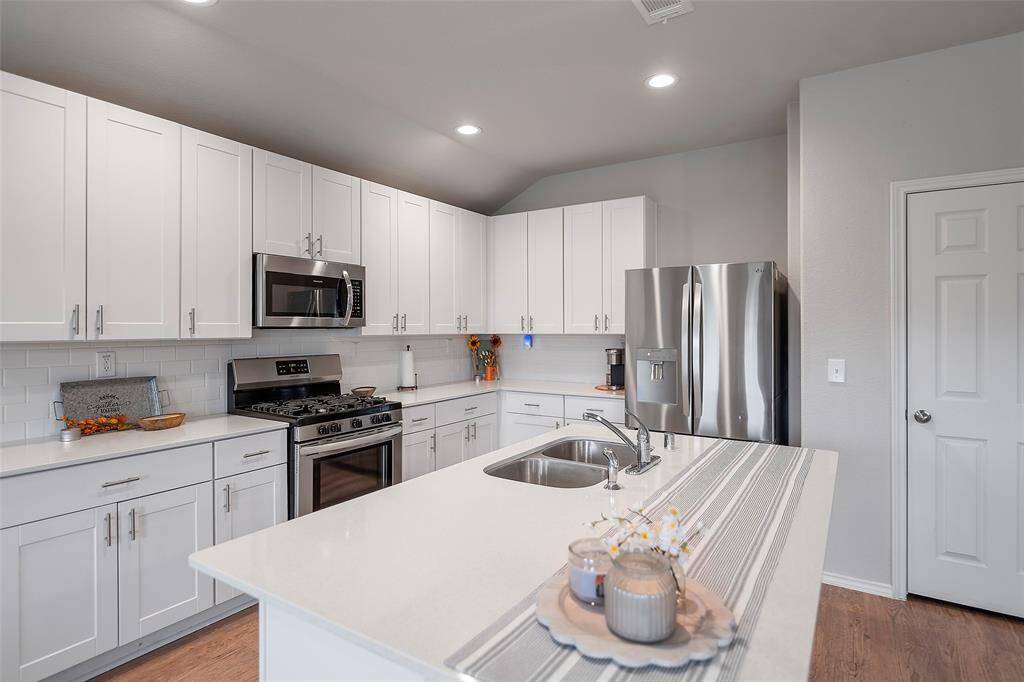 Modern kitchen featuring white cabinetry, stainless steel appliances, and subway tile backsplash, complemented by neutral countertops and ample lighting.