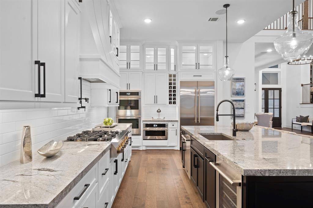 Wall-to-wall cabinetry and professional appliances line the back wall, while a sleek pot filler and built-in wine storage elevate both function and form.