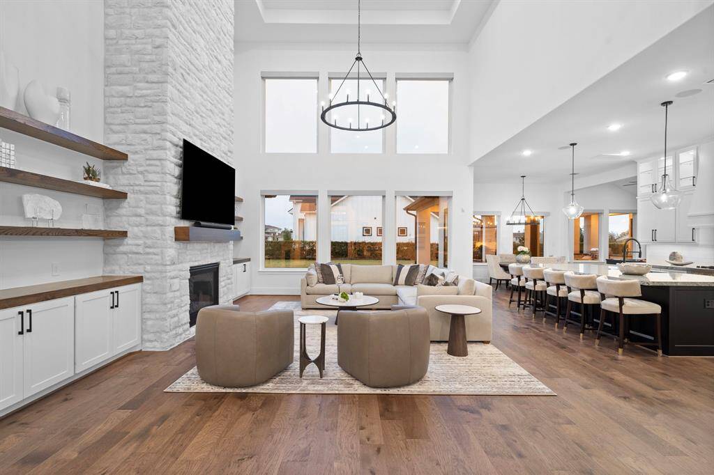 Breathtaking living area showcases soaring ceilings, expansive windows bathing the space in natural light, and elegant hardwood floors. Designer fixtures, a striking stone fireplace surrounded by built-in shelving, and seamless flow to the gourmet kitchen and covered patio create the epitome of luxury for entertaining or relaxing in style.