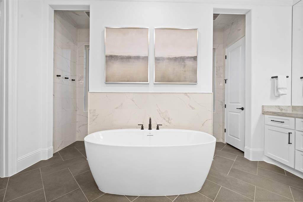 A statement tub anchors the bath, flanked by separate water closets and set against a backdrop of subtle marbled finishes.