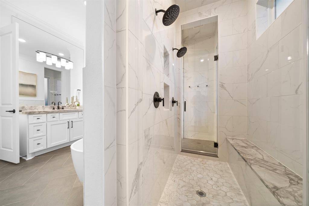 The oversized shower showcases floor-to-ceiling tilework, dual shower heads, and a built-in bench, creating a spa-caliber experience at home.