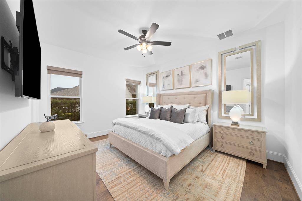 Soft natural light pours through dual windows in this serene secondary suite, featuring wide-plank hardwood floors, custom shades, and tranquil layered textures that enhance its restful ambiance.