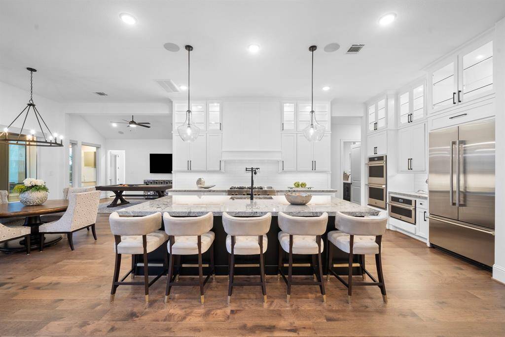 Impeccably designed gourmet kitchen features an oversized waterfall island with seating for six, sleek professional-grade stainless appliances, abundant cabinetry, and a modern tile backsplash. Pendant lighting, a spacious walk-in pantry, and the adjoining breakfast nook create both elegance and functionality, ideal for entertaining or casual dining.