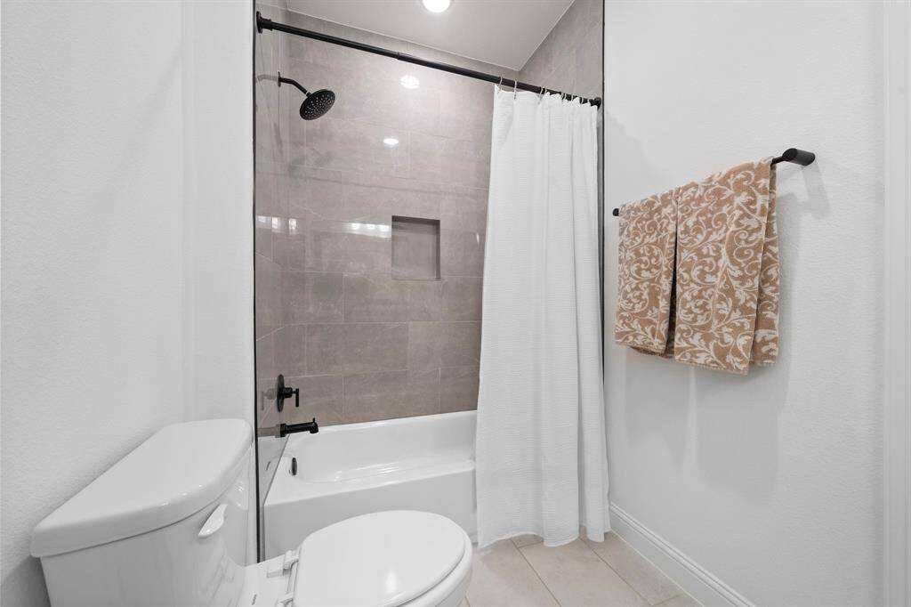 A full-height tile surround, niche shelving, and matte black fixtures complete the ensuite with polished detail.