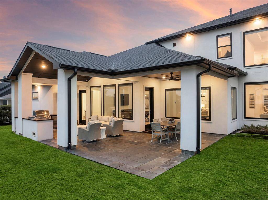 The expansive covered patio wraps the rear elevation with slate-style pavers, recessed lighting, and multiple access points for a seamless indoor-outdoor flow.