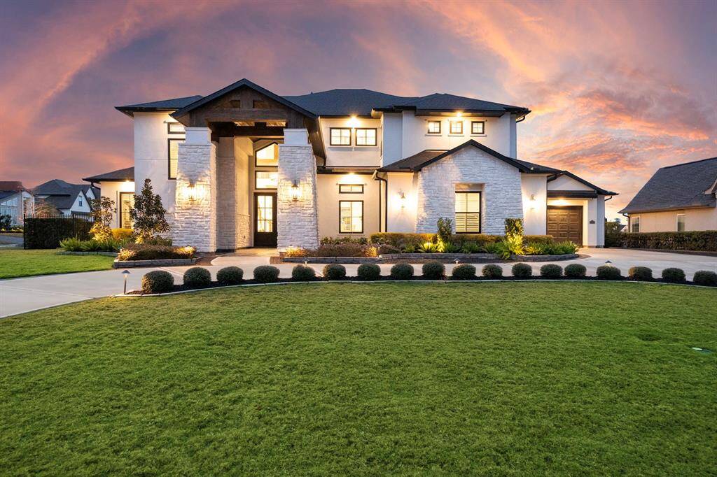 Stone columns, wood beam accents, and tiered rooflines give the exterior depth and dimension, framed by clean landscaping and architectural lighting.