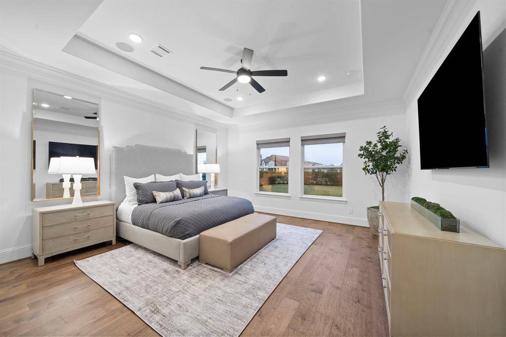 Retreat to a spacious first-floor primary suite offering serene backyard views, elegant hardwood flooring, and a sophisticated tray ceiling. High-end finishes, abundant natural light, and a custom walk-in closet create an inviting haven designed for luxury and comfort.