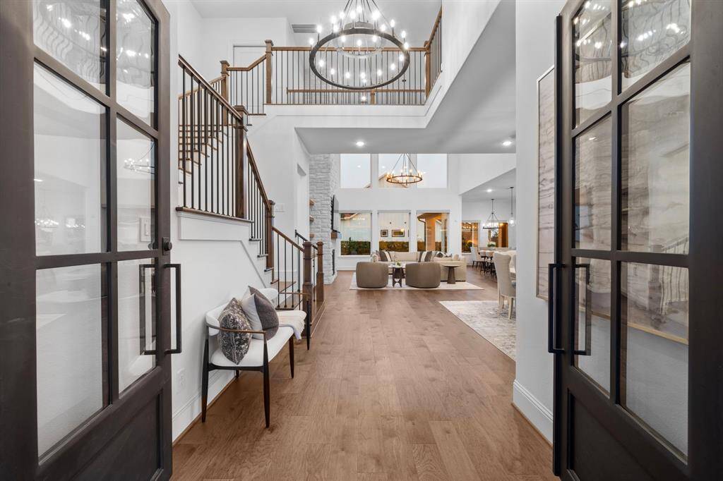 Framed by double glass doors and a soaring ceiling, the foyer opens to reveal iron-spindled stairs, warm hardwoods, and a full view into the home’s main living spaces, setting a tone of elegance from the very first step.