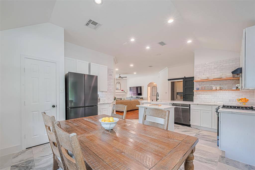 This photo showcases a bright, open-concept kitchen and dining area. It features white cabinetry, and stainless steel appliances. The kitchen has a stylish backsplash, ample counter space, and flows into a cozy living area.