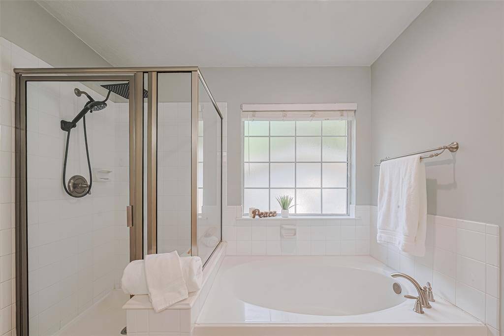 Bright and inviting bathroom featuring a glass-enclosed shower and a spacious soaking tub. The large window provides natural light, enhancing the serene atmosphere. Modern fixtures and neutral tones create a relaxing retreat.