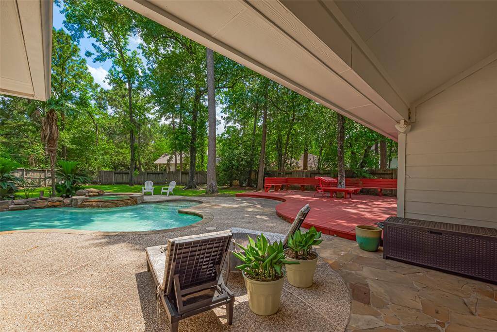 This photo shows a spacious backyard featuring a swimming pool surrounded by trees, a stone patio, and a red wooden deck with seating. It's a serene outdoor area perfect for relaxation and entertaining.