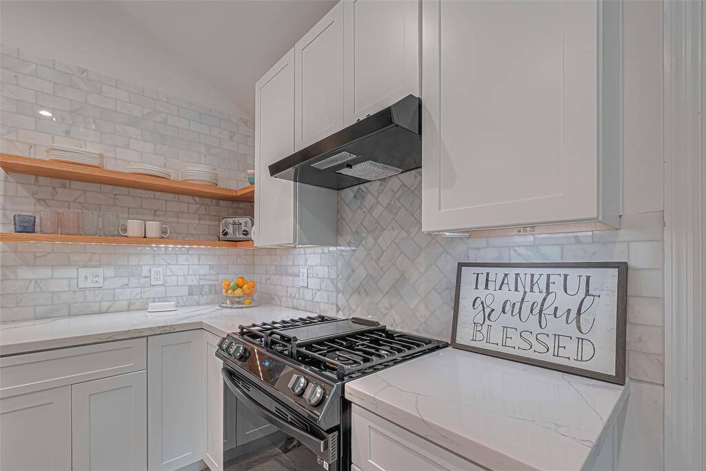 Newly renovated kitchen has new modern white cabinets, quartz countertops, marble backsplash and new range beautifully accented by the floating shelves.