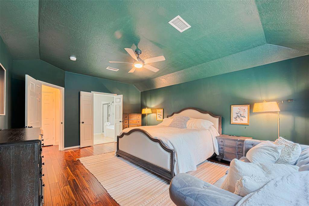 This spacious bedroom features rich green walls, a ceiling fan, and warm wood flooring. It has room for large bed, furniture and has ample natural light. A door leads to an en-suite bathroom, enhancing convenience and privacy.