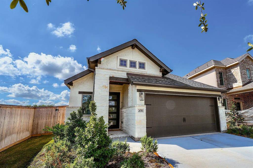 This charming home features a modern exterior with a clean, light stone finish and dark accents. It includes a two-car garage and a well-maintained front yard with lush greenery. The house is set against a backdrop of blue skies, providing a welcoming and serene atmosphere.