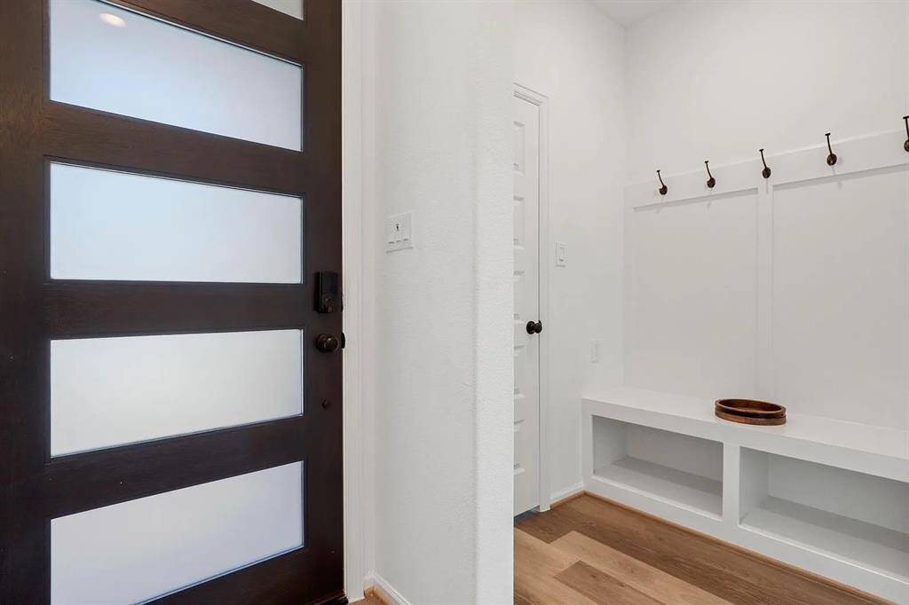 This entryway features a modern door with frosted glass panels, a bright white interior with a built-in bench, and hooks for convenient storage. Perfect for a functional and welcoming entrance.