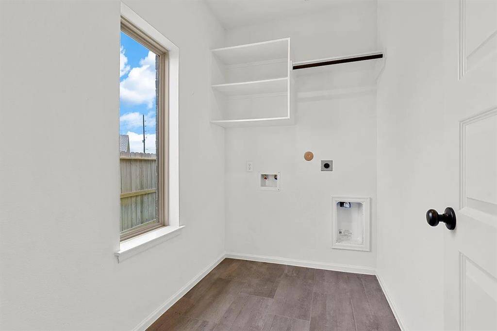 This is a bright and functional laundry room with wood flooring, a window for natural light, and built-in shelving. It has hookups for a washer and dryer.