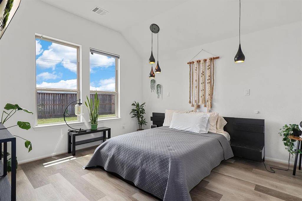 This bedroom features a modern, minimalist design with large windows providing natural light. It has  stylish hanging lights creating a cozy and inviting atmosphere.